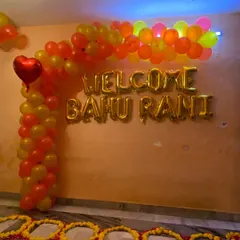 A closer look at the 'Welcome Bahu Rani' balloon arrangement. The gold foil letters stand out against the orange and yellow balloon arch, creating a festive and celebratory photo opportunity.