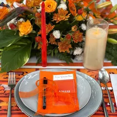 A close-up of a place setting, featuring a personalized menu and a small pen for writing wishes, all in the event's signature orange.