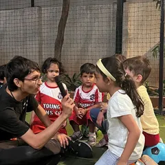 A coach kneels down to speak with a child at her level, holding a microphone to make her feel special. We believe in listening to our students and valuing their voices.