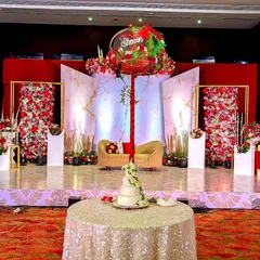 A grand reception stage with a dramatic red and white floral theme. The backdrop combines marble-finish panels with walls of flowers, creating a look of modern opulence.