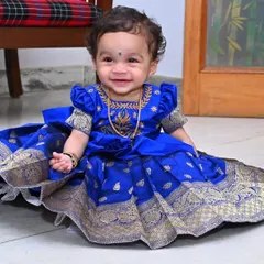A smiling little one in her bespoke Pattu Pavadai. This royal blue silk dress, adorned with traditional gold zari work and puffed sleeves, is designed for both beauty and comfort, making it ideal for cultural ceremonies, festivals, and first birthdays.
