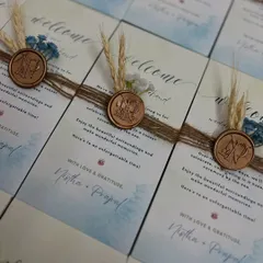 A close-up of the personalized welcome notes for the NP wedding. Each card is adorned with a custom 'NP' monogram wax seal, twine, dried wheat, and delicate flowers, offering guests a warm and heartfelt greeting upon arrival.