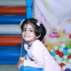 A sweet, candid portrait of a little girl enjoying the party from the colorful ball pit, a perfect example of kids' event photography.