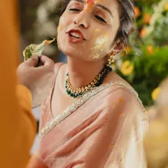 A playful moment during the Haldi ceremony, where the bride is lovingly smeared with turmeric paste. Her expression is a perfect mix of joy and mischief.