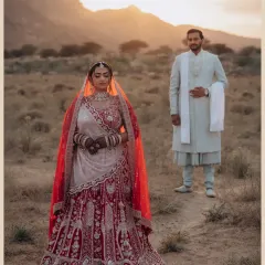 A stunning portrait of Nishi against the warm, setting sun. The golden light beautifully highlights the intricate details of her red lehenga, set against the rugged mountain landscape.