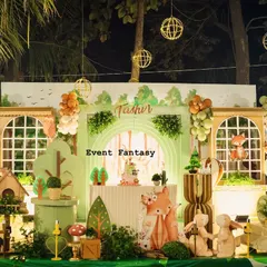 Tashvi's woodland birthday stage glowing in the evening light. The setup features a cozy house backdrop, illuminated by string lights, with cute fox and rabbit props creating a warm and inviting atmosphere.