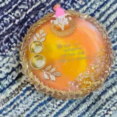 A bright and sunny pooja thali in shades of orange and yellow. It's decorated with a delicate golden lace border, silver leaf accents, and a small Ganesh idol for blessings.