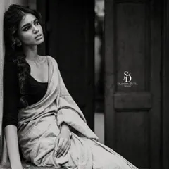 A soulful black and white portrait of a model sitting in a rustic doorway. The deep shadows and her melancholic expression give the image a cinematic and timeless quality.