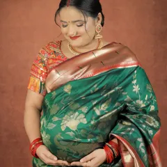 A close-up portrait focusing on the rich texture of the silk saree and the mother's gentle embrace of her baby bump.