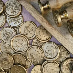 A collection of our handmade gold wax seals, ready to be applied. Each seal comes with an adhesive back for easy application and is available in various intricate designs, from olive branches to blooming poppies.