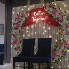 For a modern and romantic ring ceremony, we design backdrops like this one. It features a floral ring, soft drapes with fairy lights, and a custom neon sign like 'Better Together' to make your engagement stage truly personal.