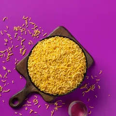 A vibrant shot of Aloo Bhujia against a solid purple background. This type of high-contrast, colorful food photography is designed to grab attention on retail shelves and online.