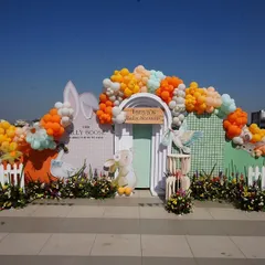 For this rooftop bunny-themed baby shower, I created a vibrant and cheerful backdrop against the open sky. The setup features a white picket fence, lush florals, and a playful balloon arch in pastel and orange tones, perfect for a sunny day.