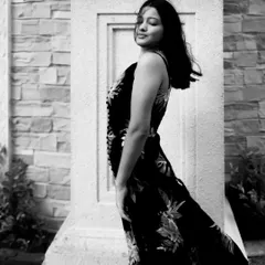 A black and white portrait using natural light and a stone pillar for framing. The motion in the model's hair adds a dynamic, candid feel to the shot.
