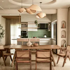 I design open-concept spaces where life flows seamlessly from one moment to the next. This view connects the dining area to the kitchen, unified by sculptural wooden pendant lights, natural materials like cane and teak, and architectural details like the recessed ceiling, demonstrating a complete and cohesive home vision.