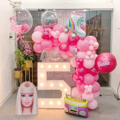 This Barbie-themed 5th birthday party setup includes a light-up marquee number '5', a pink balloon garland with a roller skate foil balloon, and iconic props like a Barbie head cutout and a retro boombox.