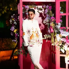 A client looking sharp in a hand-painted white jacket, posing in a floral-adorned photo booth. The jacket features artistic bird motifs, making it a standout piece that is both elegant and creative.
