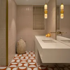 This bathroom combines soft pink vertical tiles on the walls with a bold orange and white patterned tile on the floor. A woven jute laundry basket adds a natural, textural element.
