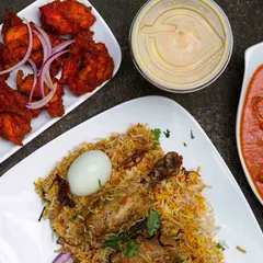 A complete Mughlai meal featuring my signature Chicken Biryani with a boiled egg, a side of rich chicken curry, spicy chicken 65 starters, and a cooling dip.