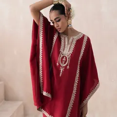 A detail-oriented shot from the Saisha lookbook, highlighting the delicate hand-embroidery on the neckline of the red kaftan. The pose and composition are directed to showcase the garment's craftsmanship and luxurious feel.
