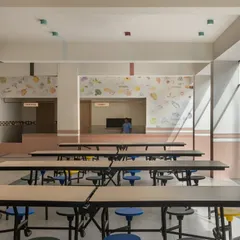 The dining hall is designed to be bright, open, and cheerful. The long tables with colorful stools encourage community, while the educational murals in the background provide food for thought.