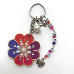 A close-up of a floral personalised keychain I made. It features a hand-painted flower, pearl embellishments, and a beaded chain with the name 'IHORA' and cute elephant and butterfly charms.