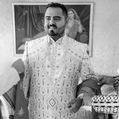 A classic black and white shot of the groom getting help with his sherwani. These moments of camaraderie with friends and family are an essential part of the day.