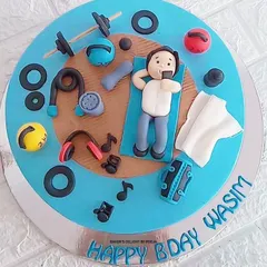 A cake for a true fitness enthusiast. This design features a fondant figure relaxing at the gym after a workout, surrounded by edible weights, kettlebells, headphones, and other gym equipment.