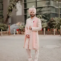 A full-length portrait of the groom looking sharp in his pastel pink sherwani. This shot shows off his complete wedding day look with elegance and style.