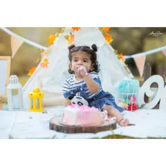 Getting right into her first birthday cake. This shot from Nitya's cake smash session shows her enjoying every moment. The setup includes a teepee, lanterns, and a "One" sign to mark the special occasion.