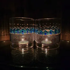 A pair of lamp chimneys with a blue geometric pattern, illuminated from within. The design is inspired by traditional motifs and looks stunning in the dark.