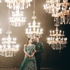 A glamorous pre-wedding portrait in a studio filled with dozens of sparkling chandeliers, creating a magical and luxurious atmosphere for this elegantly dressed couple.