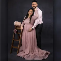 A classic couple's maternity portrait. The partner stands behind the mother-to-be, both gently holding the bump, symbolizing their shared journey and support for one another. The soft pink tones add a romantic feel.