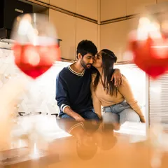 A sweet kiss on the cheek, framed by glasses of wine. An intimate moment from Prakshi and Akshay's cozy at-home pre-wedding shoot.