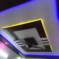 This multi-layered PVC ceiling uses a combination of dark wood and white panels. The dual-color blue and yellow lighting highlights the geometric shapes for a dynamic look.