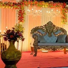 A classic stage setup for a Sangeet or reception at a farmhouse, featuring a golden throne sofa, a draped backdrop with floral borders, and elegant chandeliers.