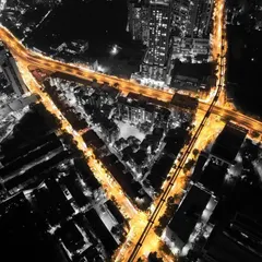 An edited top-down shot of Mumbai's roads at night, with the streets glowing in orange against a black and white city.