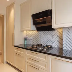 A closer view of the cooking area in a classic kitchen. This image shows the detailed cabinet profiles, sleek brass handles, and a striking herringbone tile backsplash that adds texture and character.