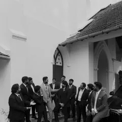 The groom shares a laugh with his groomsmen outside the church. This candid black and white shot captures the relaxed and happy atmosphere among friends before the ceremony.