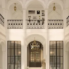 A view of the double-height lobby from the mezzanine level, showing the intricate ironwork of the balcony railings and the grand arched doorways below. This neo-classical design creates a layered and visually rich environment, typical of a five-star hotel.