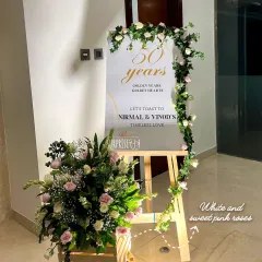 A welcome easel for a 50th anniversary, adorned with a garland of white and sweet pink roses. This was the first thing guests saw, setting a tone of timeless love for the celebration.