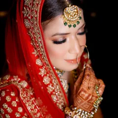 A delicate and graceful bridal portrait. The focus is on the bride's beautiful makeup, jewelry, and the intricate details of her henna.