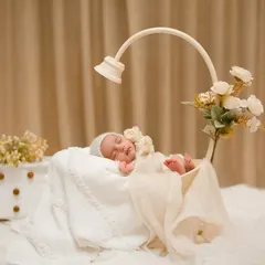 This full setup shot shows a serene, all-white theme. The soft lighting, cozy blankets, and floral details create a peaceful and angelic atmosphere for this sleeping newborn's first photoshoot.