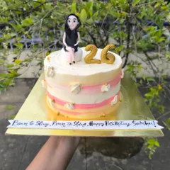 A personalized 26th birthday cake with a custom fondant figurine of the birthday girl, sitting atop a pretty pink and yellow watercolor buttercream cake.