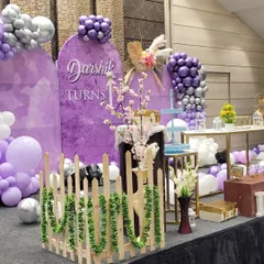 A side view of the purple-themed first birthday stage, showing the layered decor with a small picket fence, floral arrangements, and pedestals for the cake and desserts.
