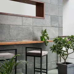 This outdoor bar area is a perfect example of bringing the indoors out. The slate stone wall continues from the living room, creating continuity, while the simple black bar stools and potted plants make it a chic, green escape.