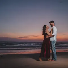 A full-length portrait of a couple on the beach at dusk. The deep colors of the sky and her velvet dress create a dramatic, cinematic feel.