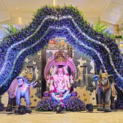 A majestic Ganesha installation for a wedding ceremony. The large idol is framed by an arch of purple flowers and flanked by two decorated elephants, creating a powerful and blessed focal point.