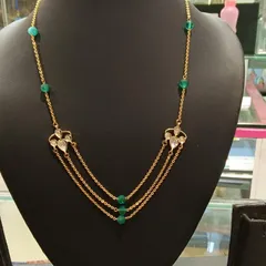 A modern, layered necklace design. This piece features three delicate gold chains accented with green beads and small Kundan motifs, creating a trendy look.