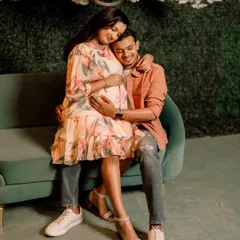 A sweet and tender portrait of an expecting couple on a green sofa. The focus is on their happy expressions and the gentle way they hold the baby bump.